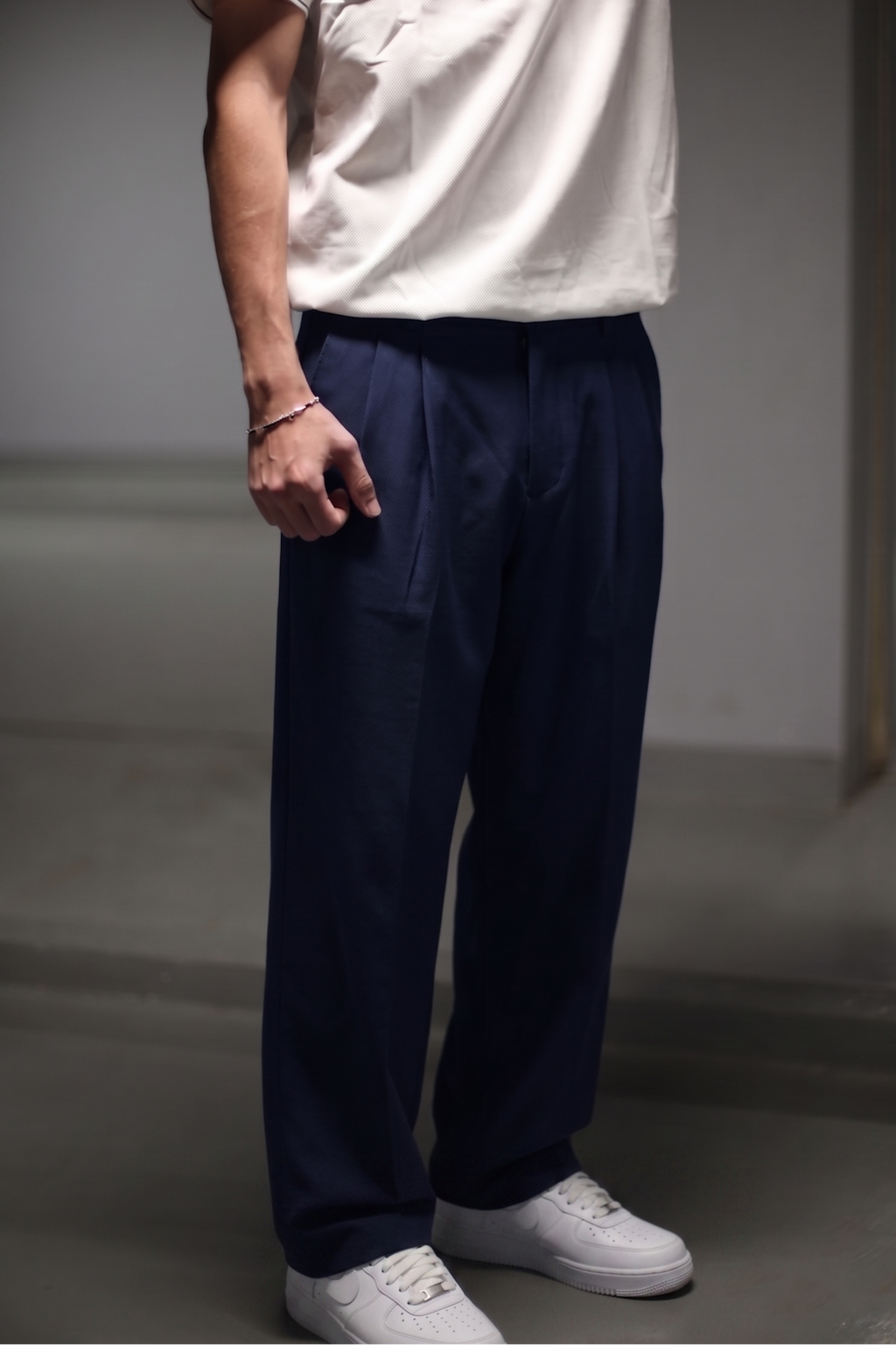 Person wearing a white t-shirt and navy pants in a minimalistic setting